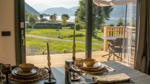 Udsigt fra et glamping-ophold med dækket spisebord, terrasse og bjergsø i baggrunden.