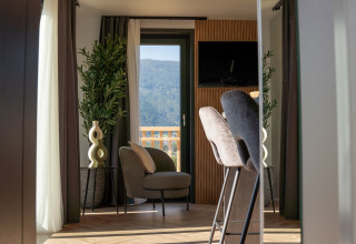 Moderne glamping-indkvartering med stilfuld stue, udsigt til bjerge, grønne planter og store vinduer.