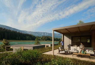 Glamping cabins by a lake in a holiday park, surrounded by mountains and forest, with guests on the terrace.