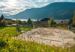 Terrain de volley sur sable dans un parc de vacances glamping, vue sur lac et montagnes en soirée.