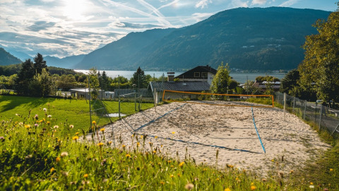 Strandvolleyballbane ved en sø og bjerge, set fra en feriepark med glamping, under en dramatisk himmel.