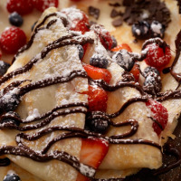 Deliciosos crepes con salsa de chocolate, frutos rojos frescos y un toque de azúcar glas.