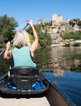 Mujer remando en canoa por un río tranquilo con árboles y un castillo al fondo en un parque de vacaciones.