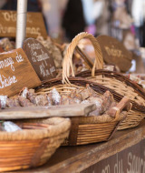 Puesto de mercado con cestas repletas de embutidos tradicionales y carteles escritos a mano en francés.