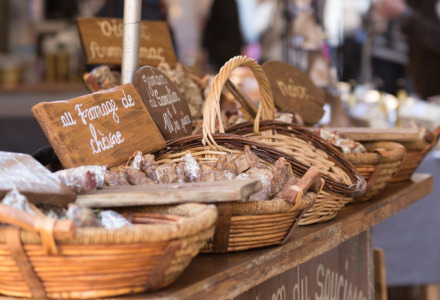 Puesto de mercado con cestas repletas de embutidos tradicionales y carteles escritos a mano en francés.