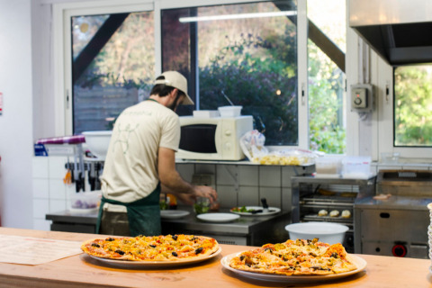 Cocinero preparando comida en una cocina con pizzas en el mostrador en Huttopia Saumur, Pays de la Loire, Francia.
