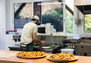 Kok aan het werk in keuken met pizza's op de toonbank bij Huttopia Saumur, Pays de la Loire, Frankrijk.