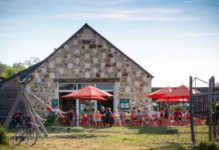Buiten café met rode parasols en spelende kinderen bij Huttopia Saumur in Pays de la Loire, Frankrijk.