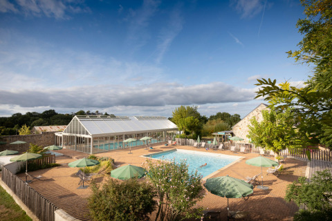 Piscina al aire libre con tumbonas y sombrillas verdes en Huttopia Saumur, parque vacacional en Pays de la Loire, Francia.