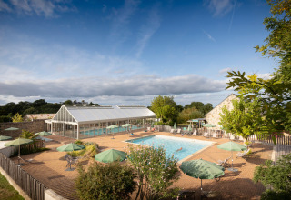 Outdoor swimming pool with sun loungers and green umbrellas at Huttopia Saumur holiday park, Pays de la Loire, France.