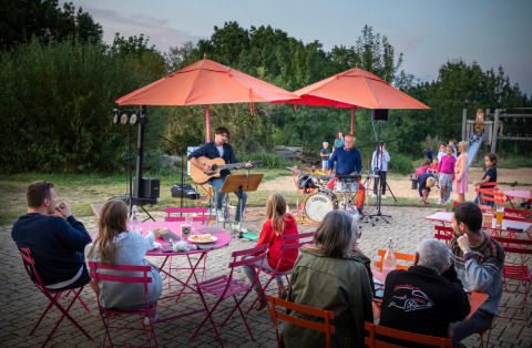 Live muziekoptreden buiten bij Huttopia Saumur, gezinnen eten aan tafels en kinderen spelen op de achtergrond.