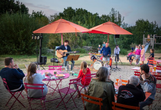 Udendørs musikoptræden ved Huttopia Saumur feriepark, gæster nyder maden og børn leger i baggrunden.
