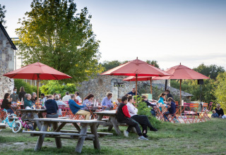 Buiten tafelen aan picknickbanken met rode parasols bij Huttopia Saumur vakantiepark in Pays de la Loire.