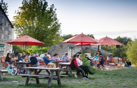 Mensen dineren buiten aan picknicktafels met rode parasols bij Huttopia Saumur vakantiepark in Pays de la Loire.