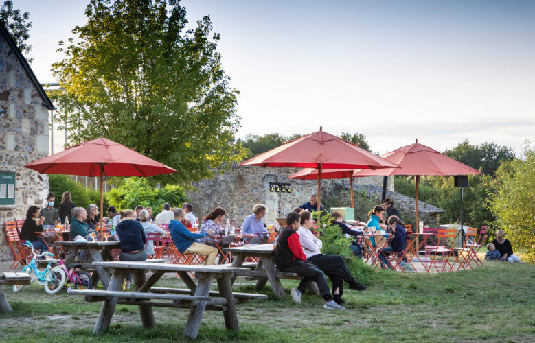 Mensen dineren buiten aan picknicktafels met rode parasols bij Huttopia Saumur vakantiepark in Pays de la Loire.