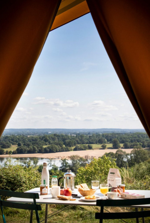 Breakfast outside a tent overlooking the river and scenic landscape at Huttopia Saumur, Pays de la Loire, France.