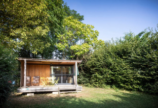 Houten chalet met overdekt terras en tuinmeubelen in het groen bij Huttopia Saumur, Pays de la Loire.