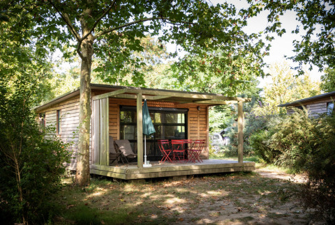 Cabaña de madera con porche y muebles rojos en Huttopia Saumur, parque vacacional en Pays de la Loire, Francia.