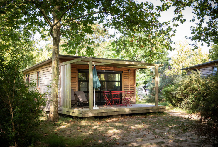 Wooden cabin with shaded porch and red patio furniture at Huttopia Saumur holiday park in Pays de la Loire, France.