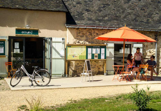 Mensen zitten onder een oranje parasol aan de receptie van Huttopia Saumur, Pays de la Loire, Frankrijk.