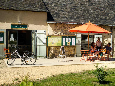 Menschen sitzen unter einem orangefarbenen Sonnenschirm vor der Rezeption von Huttopia Saumur in Pays de la Loire.