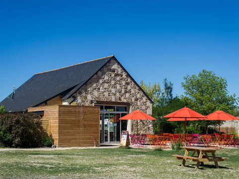 Zona de cafetería al aire libre con sombrillas coloridas en Huttopia Saumur en Pays de la Loire, Francia.