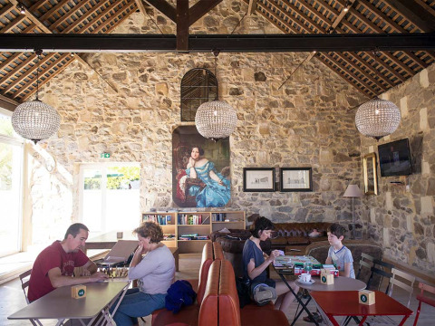 Familias disfrutan de juegos de mesa en un salón de paredes de piedra y lámparas en Huttopia Saumur.