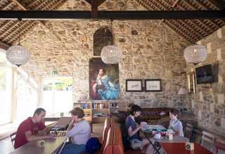 Des familles jouent dans un salon chaleureux avec murs en pierre et lustres au Huttopia Saumur, France.