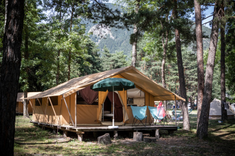 Foto van een safaritent op een bosrijke camping met uitzicht op bergen en stoelen op de veranda.