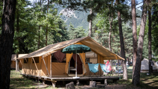 Foto di una tenda safari in un campeggio boscoso con vista montagna, sedie a sdraio e alberi intorno.