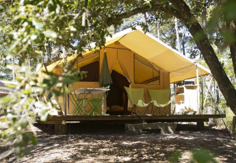 Tenda safari con veranda immersa tra gli alberi, perfetta per una vacanza di glamping nella natura.