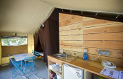 Interior view of a Toile&Bois tent Sweet safari tent with kitchen area, dining table, and sleeping cabin.