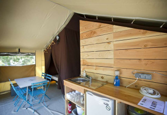 Vue intérieure d’une tente safari Toile&Bois tent Sweet avec coin cuisine, table à manger et cabine de couchage.