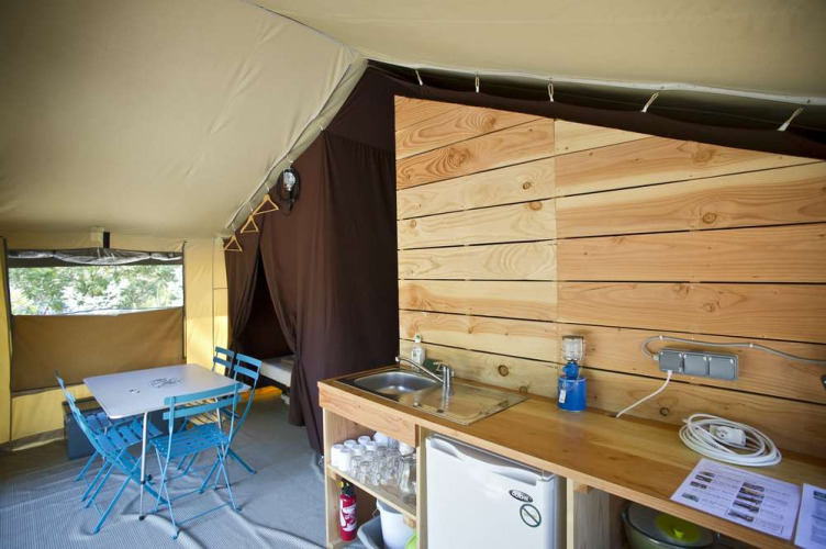 Interior view of a Toile&Bois tent Sweet safari tent with kitchen area, dining table, and sleeping cabin.