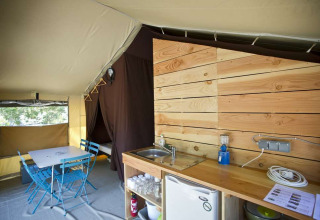 Vue intérieure d’une tente safari Toile&Bois tent Sweet avec coin cuisine, table à manger et cabine de couchage.