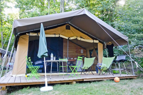 Safari-Zelt Toile&Bois tent Sweet auf Holzterrasse, umgeben von Bäumen, mit Campingmöbeln davor.