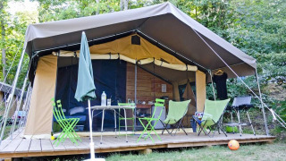 Safari tent Toile&Bois tent Sweet op houten terras, stoelen, tafel en groene bosrijke omgeving.