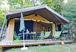 Safari-Zelt Toile&Bois tent Sweet auf Holzterrasse, umgeben von Bäumen, mit Campingmöbeln davor.