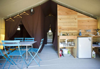Interieur van Toile&Bois Sweet safaritent met blauwe stoelen, keukentje, minicoolkast en slaapruimtes.