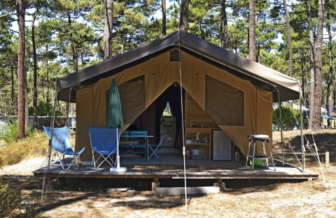 Tenda safari Toile&Bois Sweet con veranda in legno, sedie pieghevoli e ambiente nella pineta soleggiata.