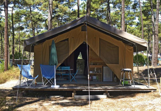 Safari tent Toile&Bois Sweet met houten veranda, klapstoelen en bosrijke sfeer tussen dennenbomen.