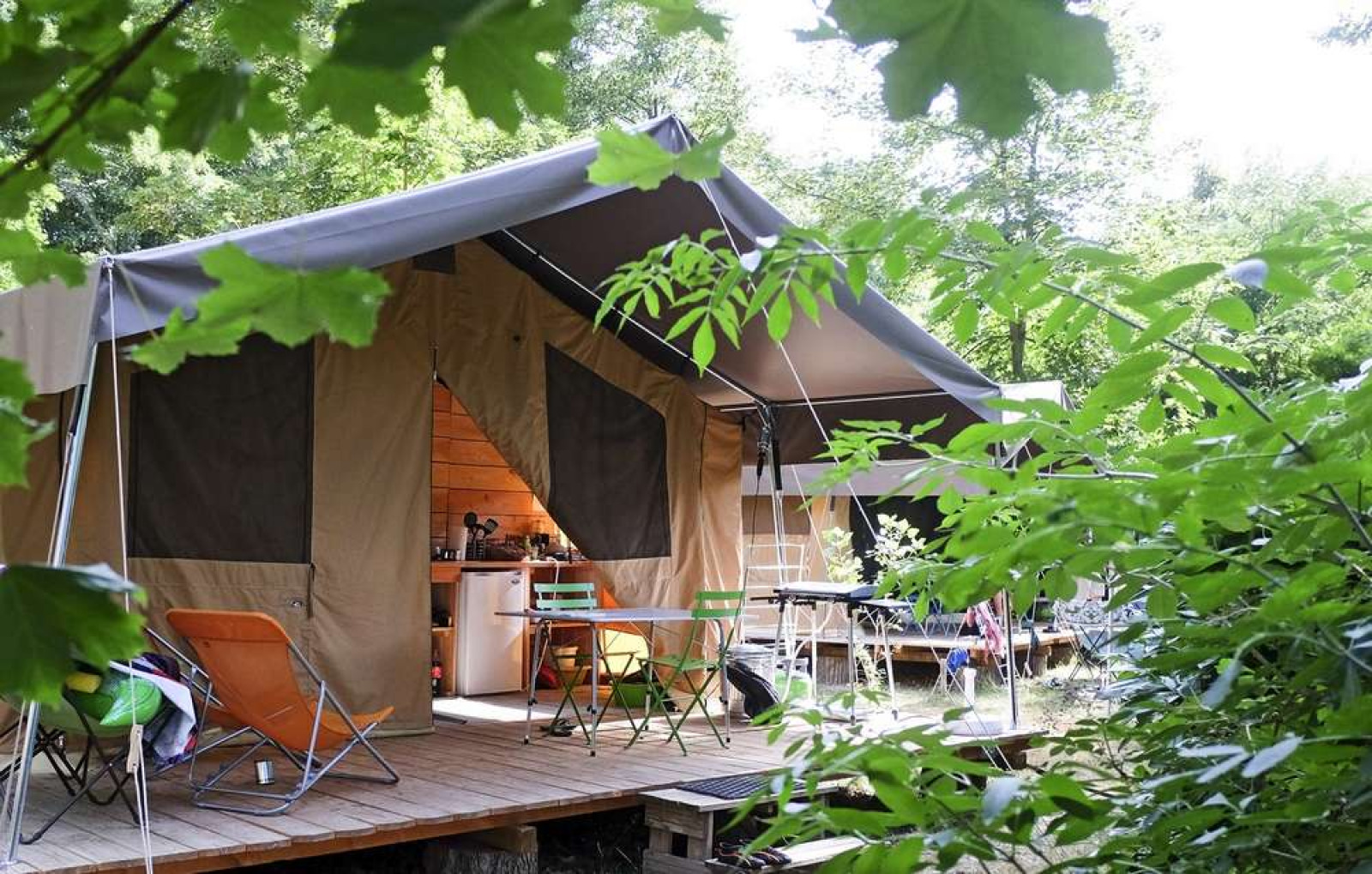 Safari-tent Toile&Bois Sweet met veranda, stoelen en tafel te midden van groene natuur en bomen.