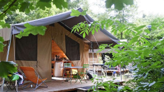 Tente safari Toile&Bois Sweet dans la nature avec terrasse, chaises et table, entourée de verdure.