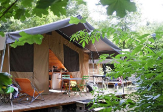 Tenda safari Toile&Bois Sweet nella natura con terrazza, sedie e tavolo, circondata dal verde.