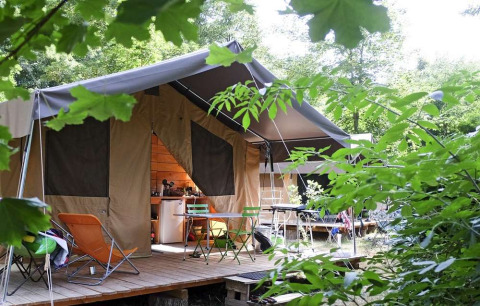 Tente safari Toile&Bois Sweet dans la nature avec terrasse, chaises et table, entourée de verdure.