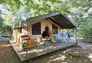Safari telt Toile&Bois Sweet med træterrasse, udendørs stole og grøn natur omkring campingpladsen.