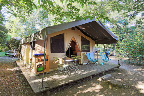 Tente safari Toile&Bois Sweet avec terrasse en bois, chaises extérieures et verdure sur un camping.