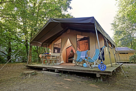 Safari-Zelt Toile&Bois Sweet auf Holzplattform im Wald, Campingmöbel davor, entspannte Atmosphäre.