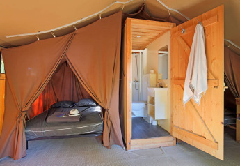 Indvendigt billede af en Safari Toile&Bois telt Sweet med seng, badeværelse og trædør.