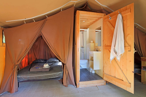 Innenaufnahme eines Safari-Toile&Bois-Zeltes Sweet mit Bett, Badezimmer und Holztür.